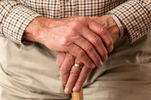 Älterer Mann überschlägt seine Hände auf seiner Gehhilfe und trgät einen auffälligen goldenen Ring am Finger